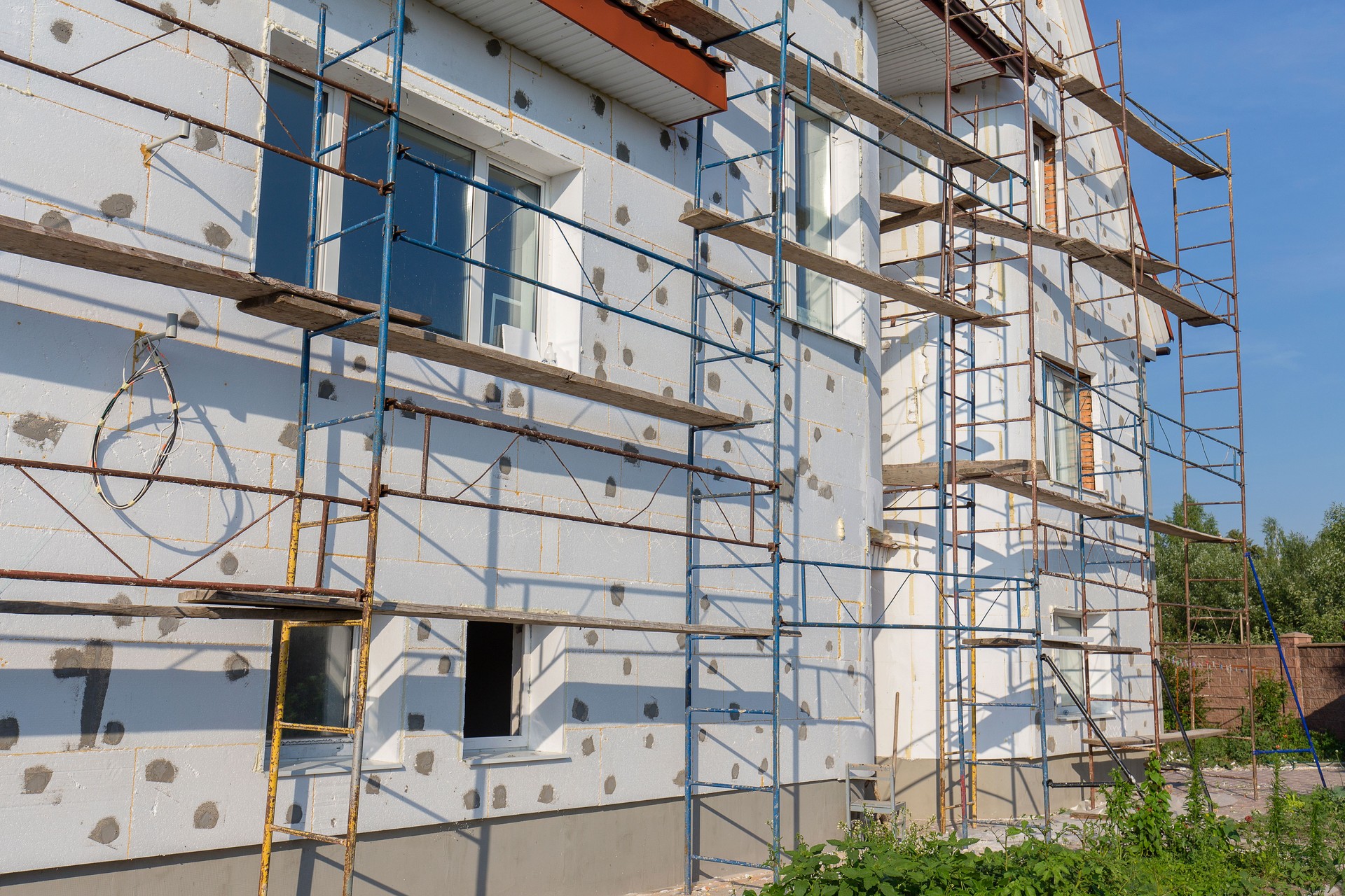 El proceso de construcción de aislamiento de la pared usando poliestireno al aire libre. Andamios en casa, renovación. Casa para restauración con el andamiaje para los trabajadores en la construcción de
